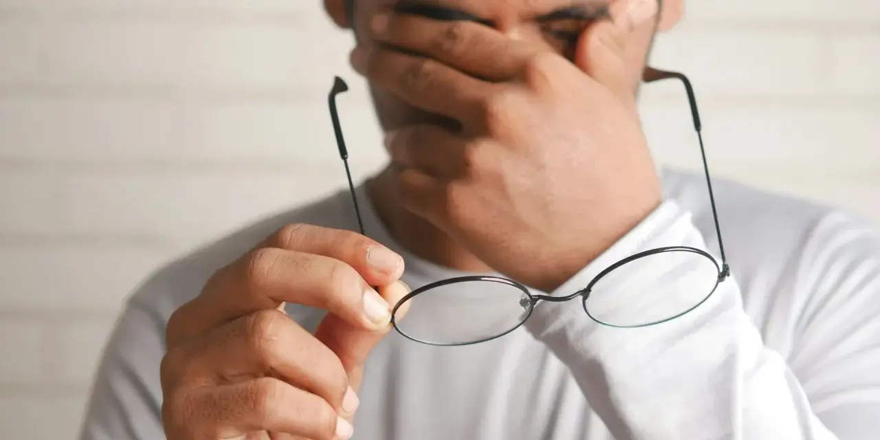 Zmęczony pracownik pociera oczy, trzymając okulary. Marzy o urlopie bezpłatnym zgodnie z kodeksem pracy.