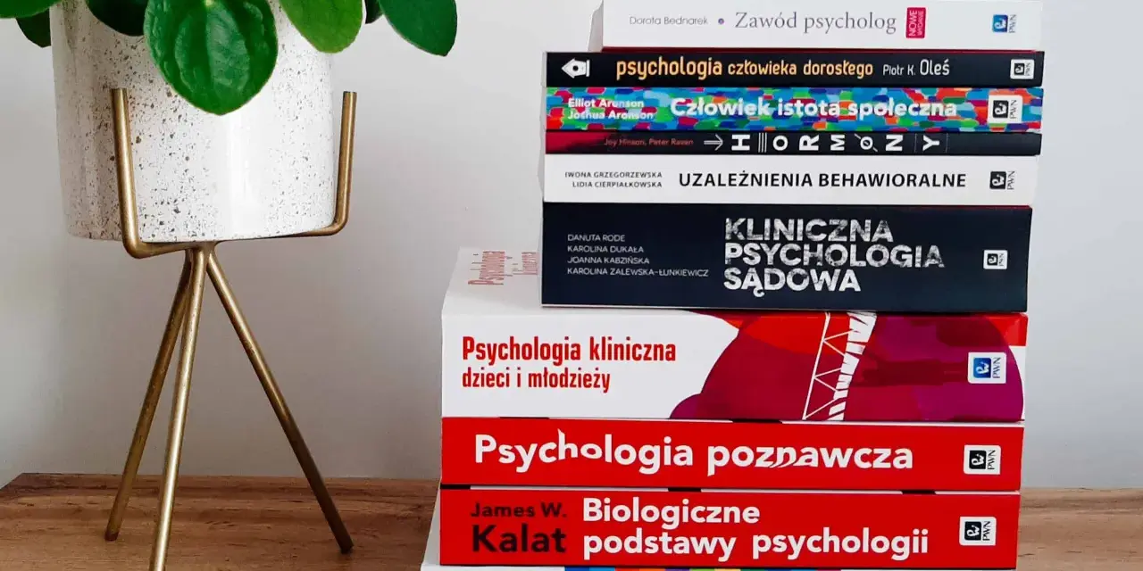 Stos książek o psychologii, od ogólnych po specjalistyczne, sugeruje, ile trwają studia psychologiczne. Obok zielona roślina.