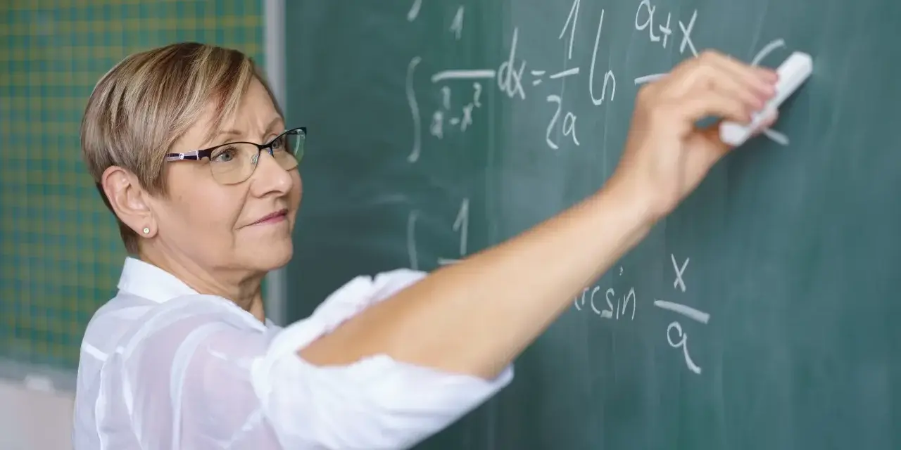 Nauczycielka matematyki pisze na tablicy wzory. Czy to zapowiedź podwyżki dla nauczycieli? Najnowsze wiadomości.
