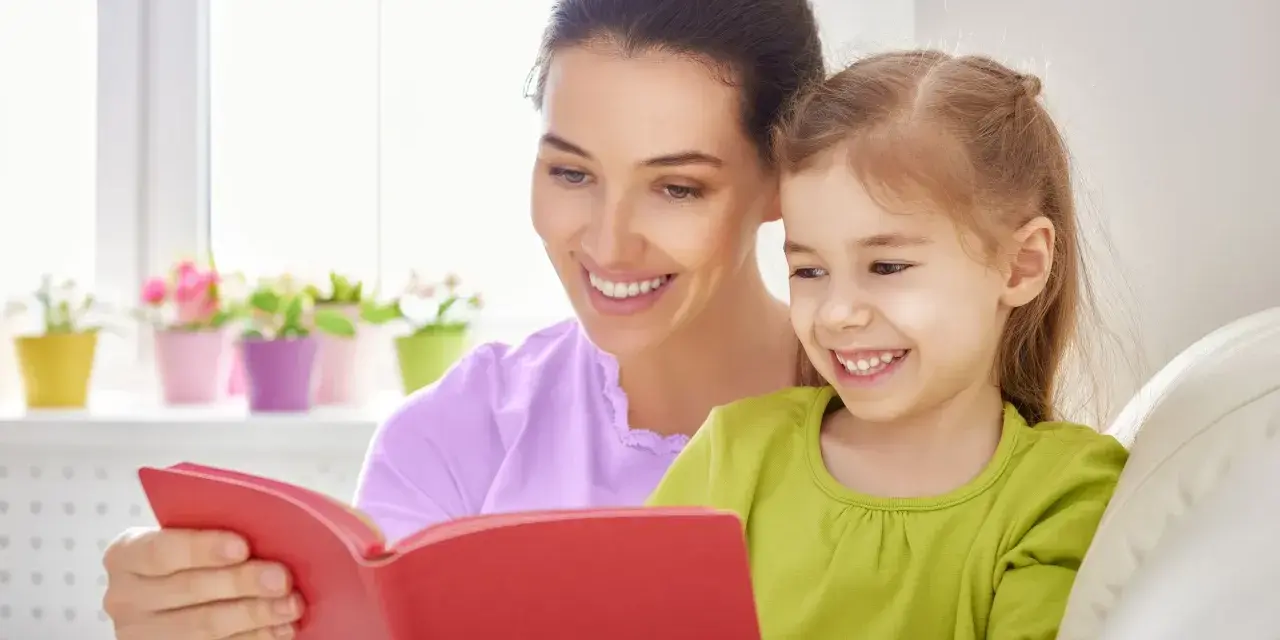 Uśmiechnięta mama czyta bajkę córce. To wspaniała opieka na dziecko 2 dni w tygodniu, pełna radości i wspólnych chwil.