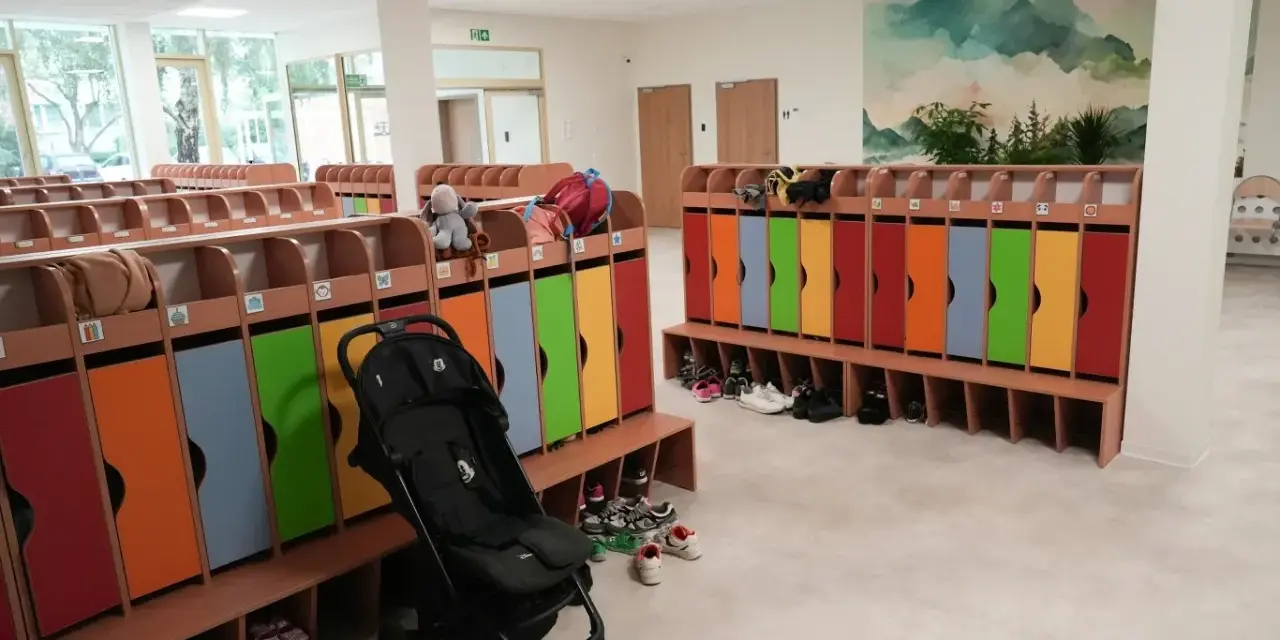 Kolorowe szafki i ławki w zespole szkolno-przedszkolnym, gotowe na przyjęcie dzieci. Wózek spacerowy czeka na swojego małego pasażera.