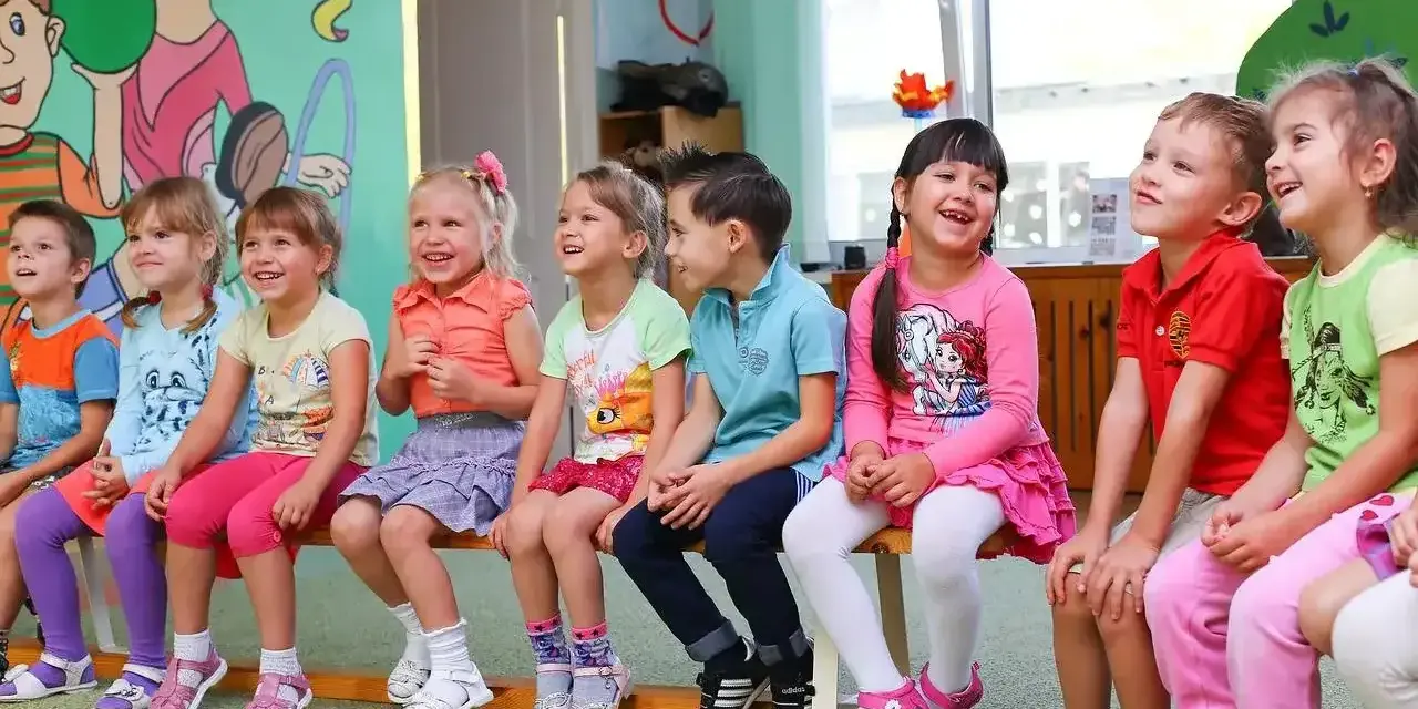 Uśmiechnięte dzieci siedzą w przedszkolu. Od ilu lat można tu uczęszczać?