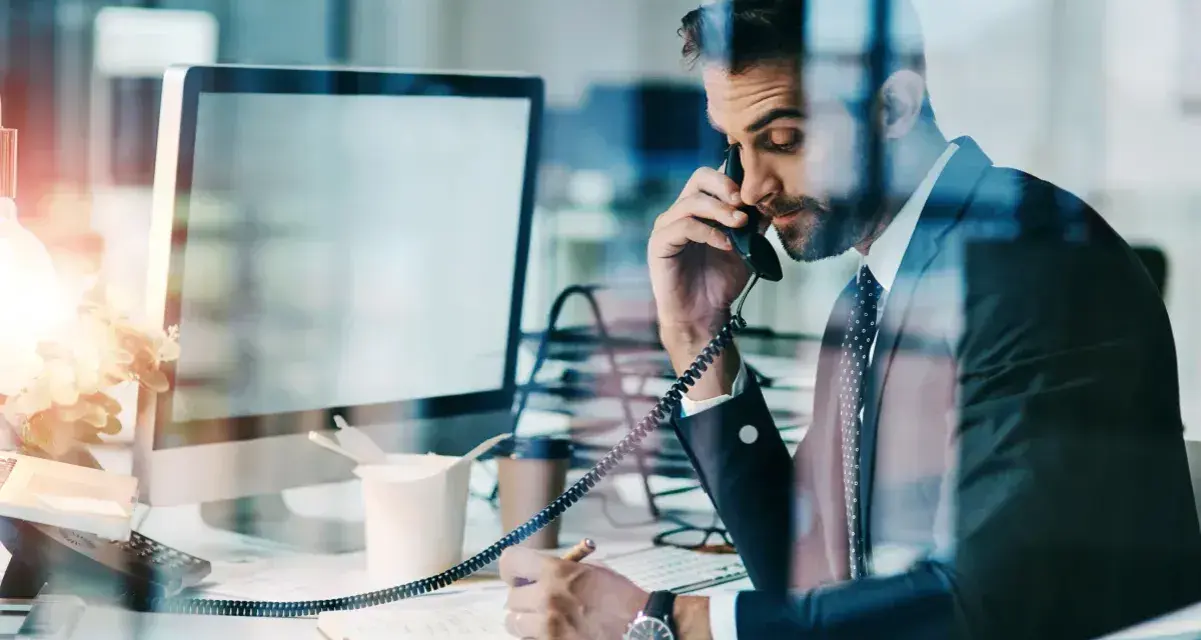 Biznesmen w garniturze rozmawia przez telefon, notując w zeszycie. Nawet w obliczu siły wyższej, praca wre.