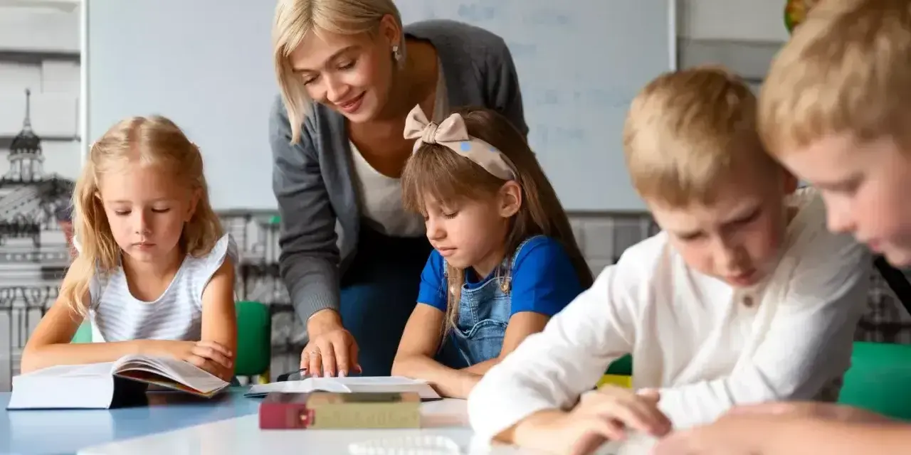 Uśmiechnięta nauczycielka wspiera dzieci w nauce. To praca, którą wykonuje oligofrenopedagog, pomagając maluchom rozwijać się.