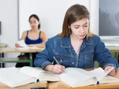 Dziewczyna w dżinsowej kurtce pisze notatki, przygotowując się do egzaminu poprawkowego.