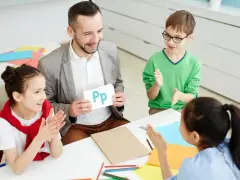 Nauczyciel pokazuje literę "Pp" podczas zebrania z rodzicami. Dzieci klaszczą, ucząc się alfabetu.