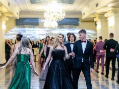 Młoda para w eleganckich strojach, ona w czarnej sukni, on w garniturze, idzie na bal studniówkowy.