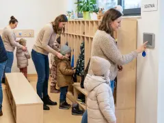 Rodzice z dziećmi w szatni, przygotowujący się do wyjścia. System kontroli zarządczej ułatwia zarządzanie wejściami i wyjściami.