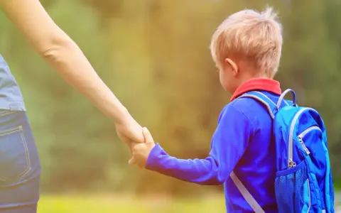 Mały chłopiec z plecakiem idzie za rękę z dorosłym. Czas na rekrutację do przedszkoli 2026!