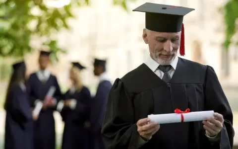 Starszy pan w todze z dyplomem zastanawia się, czy studia liczą się do stażu pracy. W tle inni absolwenci.