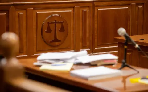 Sądowa sala z symbolem wagi sprawiedliwości i stosem dokumentów, zapewniająca zgodność z oryginałem.