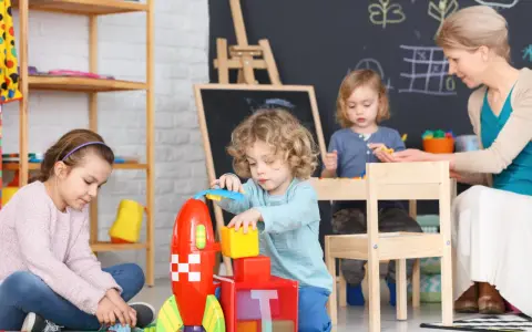 Opiekunka dziecięca z dziećmi buduje rakietę z klocków.