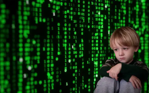 Smutny chłopiec siedzi przed ekranem z zielonym kodem, symbolizującym cyberprzemoc.