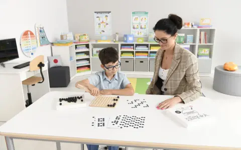 Chłopiec z nauczycielem podczas zajęć dydaktycznych z wykorzystaniem koralików i planszy.