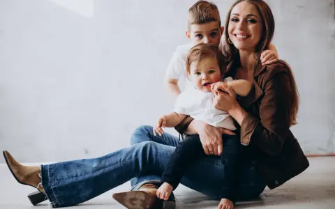 Szczęśliwa mama z dwójką dzieci, maluszkiem na rękach i starszym synkiem za plecami. Idealny urlop na dziecko.