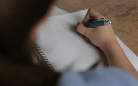 Uczeń pisze w zeszycie, zastanawiając się, ile trwa egzamin ósmoklasisty.