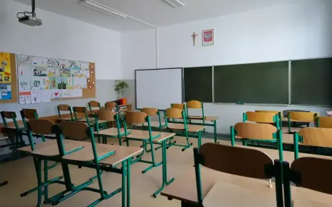 Pusta klasa szkolna z ławkami i krzesłami. Na ścianie tablica, projektor i dziecięce rysunki. Dziś odwołane zajęcia w szkołach.