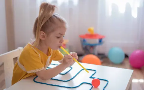 Dziewczynka ćwiczy mowę, dmuchając przez słomkę, co jest częścią terapii na dyslalię wieloraką.