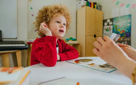 Chłopiec z kręconymi włosami, dziecko autystyczne, uczy się z kart obrazkowych.