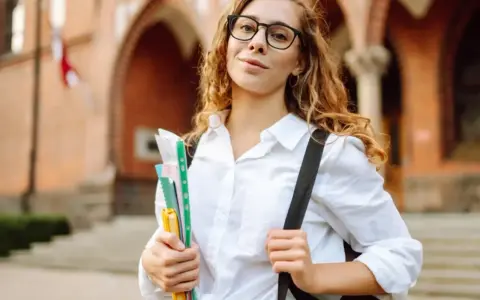 Studentka z okularami i zeszytami, gotowa do nauki. Jej klasyfikacja jako pilnej uczennicy jest oczywista.
