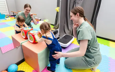 Dwie małe dziewczynki bawią się interaktywną kostką, a fizjoterapeutka wspiera ich rozwój. Www.