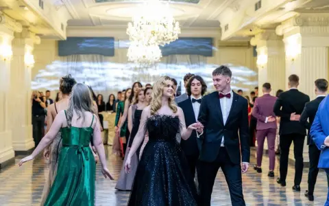 Młoda para w eleganckich strojach, ona w czarnej sukni, on w garniturze, idzie na bal studniówkowy.