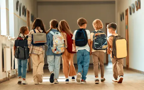 Siedmioro dzieci z plecakami idzie korytarzem szkolnym, ciesząc się ostatnimi dniami wolnymi od szkoły.