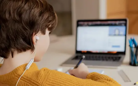 Chłopiec w żółtym swetrze uczy się zdalnie, pisząc notatki. Czy uczniowie dostaną laptopy, by móc tak pracować?