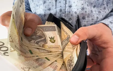 Ręce trzymają portfel z banknotami 200 zł. To symboliczne przedstawienie nagrody jubileuszowej za 15 lat pracy.