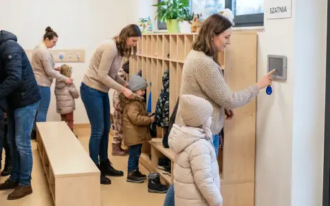 Rodzice z dziećmi w szatni, przygotowujący się do wyjścia. System kontroli zarządczej ułatwia zarządzanie wejściami i wyjściami.