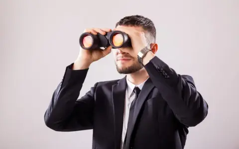 Mężczyzna w garniturze przez lornetkę szuka odpowiedzi na pytanie: wakat co to.