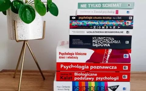 Stos książek o psychologii, od ogólnych po specjalistyczne, sugeruje, ile trwają studia psychologiczne. Obok zielona roślina.