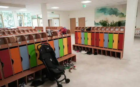 Kolorowe szafki i ławki w zespole szkolno-przedszkolnym, gotowe na przyjęcie dzieci. Wózek spacerowy czeka na swojego małego pasażera.