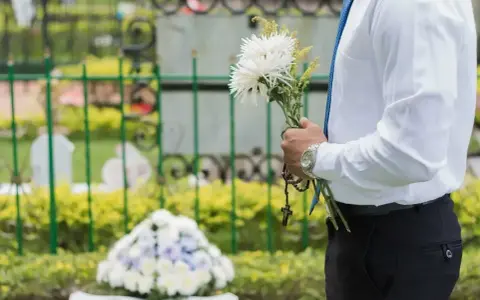 Mężczyzna w białej koszuli i niebieskim krawacie trzyma bukiet białych kwiatów i różaniec. To jego urlop okolicznościowy śmierć teścia.