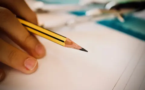 Dłoń trzymająca ołówek nad kartką papieru, symbol wsparcia w edukacji, w tym dla osób ze specjalnymi potrzebami edukacyjnymi.