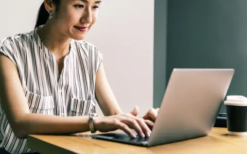 Kobieta uśmiecha się, pracując przy laptopie. Jej przygotowanie pedagogiczne online przebiega sprawnie.