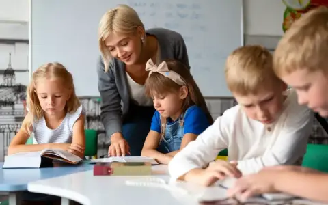 Uśmiechnięta nauczycielka wspiera dzieci w nauce. To praca, którą wykonuje oligofrenopedagog, pomagając maluchom rozwijać się.