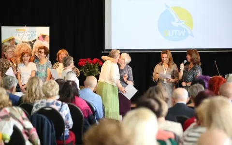 Uroczystość w Sopockim Uniwersytecie Trzeciego Wieku. Uśmiechnięci seniorzy, wręczanie dyplomów, wystąpienie.