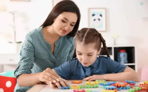 Nauczycielka wspiera dziewczynkę z niepełnosprawnością intelektualną w stopniu lekkim, układającą kolorowe puzzle.