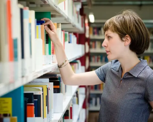 Kobieta, która wygląda jak bibliotekarz, wybiera książkę z półki w bibliotece.