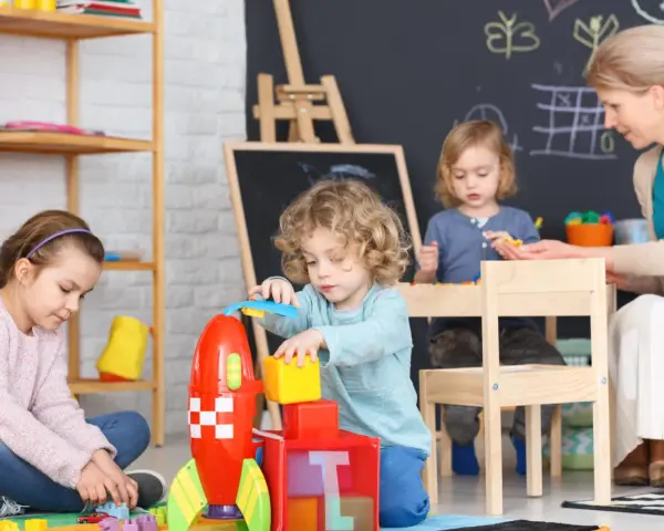 Opiekunka dziecięca z dziećmi buduje rakietę z klocków.