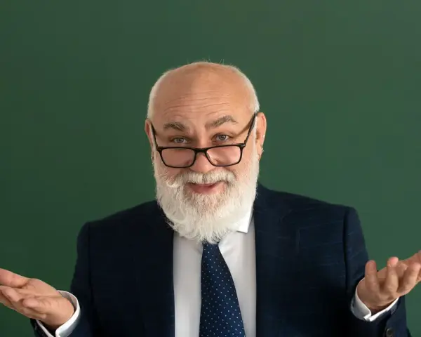 Uśmiechnięty starszy pan z brodą, w okularach i garniturze, gestykuluje, jakby wyjaśniał świadczenie kompensacyjne.