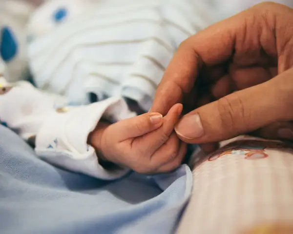 Dłoń rodzica obejmuje maleńką dłoń dziecka. To symbol miłości i troski, a także przygotowań do złożenia wniosku o urlop macierzyński.