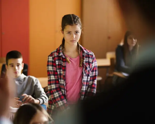 Dziewczynka w kratę czeka na swoje oceny z zachowania, wpatrując się w nauczyciela.