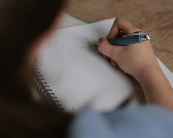 Uczeń pisze w zeszycie, zastanawiając się, ile trwa egzamin ósmoklasisty.