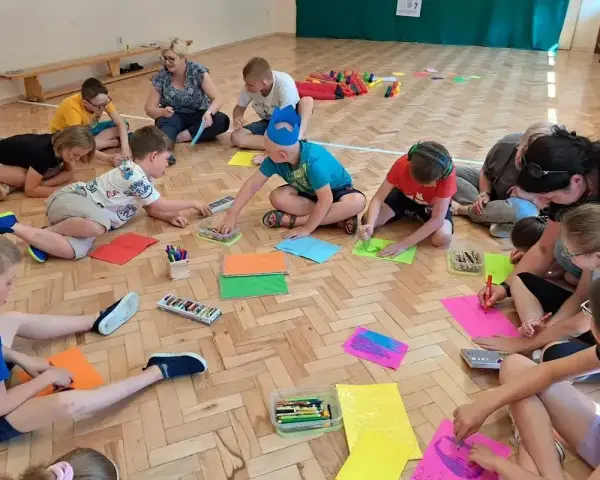 Dzieci klas 1-3 biorą udział w zabawach integracyjnych, rysując na kolorowych kartkach.