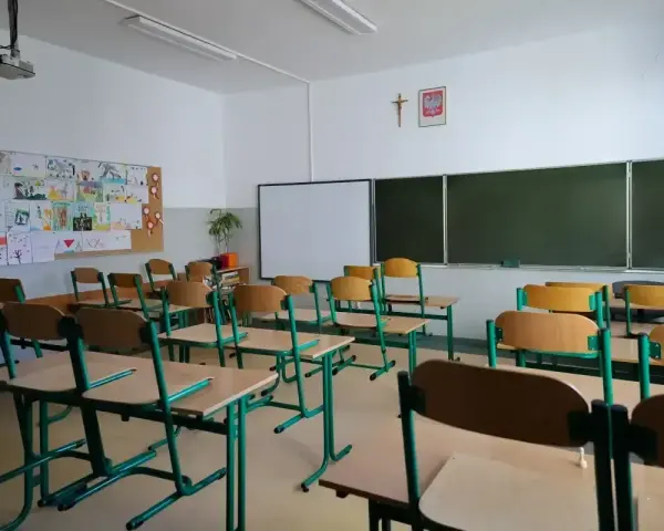 Pusta klasa szkolna z ławkami i krzesłami. Na ścianie tablica, projektor i dziecięce rysunki. Dziś odwołane zajęcia w szkołach.