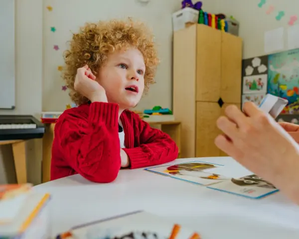 Chłopiec z kręconymi włosami, dziecko autystyczne, uczy się z kart obrazkowych.