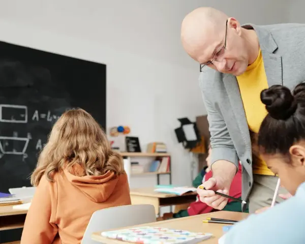 Nauczyciel pomaga uczniom podczas zajęć dydaktyczno wyrównawczych. Na tablicy wzory matematyczne.