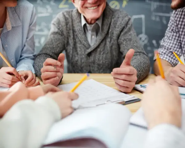 Uśmiechnięty nauczyciel w stanie nieczynnym, otoczony przez studentów piszących notatki.